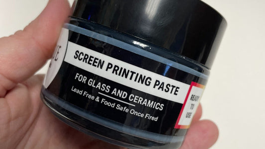 Close-up of a hand holding a jar of Rogue Screen Printing Paste labeled for glass and ceramics, lead-free and food-safe once fired.